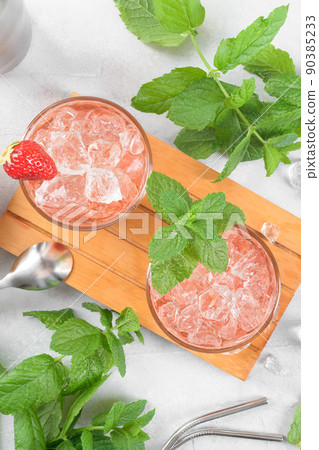 Cold strawberry cocktail mojito, margarita, daiquiri in two glasses with mint, ice and bartender tools on light table Cold strawberry cocktail mojito, margarita, daiquiri in two glasses with mint, ice and bartender tools on light table 90385233