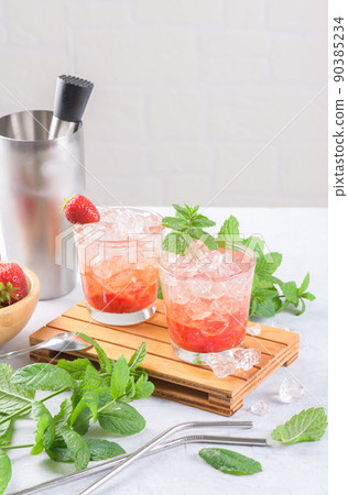 Cold strawberry cocktail mojito, margarita, daiquiri in two glasses with mint, ice and bartender tools on light table Cold strawberry cocktail mojito, margarita, daiquiri in two glasses with mint, ice and bartender tools on light table 90385234