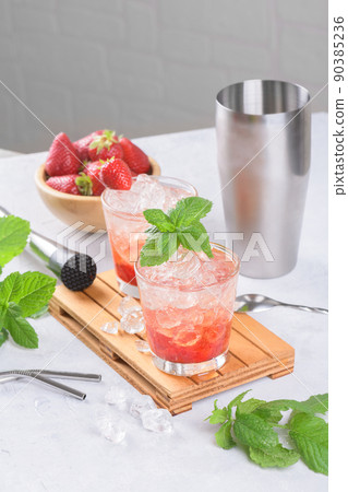 Cold strawberry cocktail mojito, margarita, daiquiri in two glasses with mint, ice and bartender tools on light table Cold strawberry cocktail mojito, margarita, daiquiri in two glasses with mint, ice and bartender tools on light table 90385236
