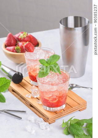 Cold strawberry cocktail mojito, margarita, daiquiri in two glasses with mint, ice and bartender tools on light table Cold strawberry cocktail mojito, margarita, daiquiri in two glasses with mint, ice and bartender tools on light table 90385237