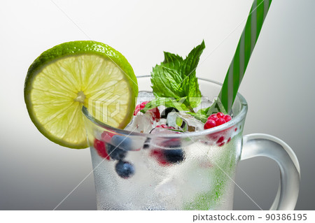 Refreshing summer cocktail with ice, lime and berries in a glass with a straw Refreshing summer cocktail with ice, lime and berries in a glass with a straw 90386195