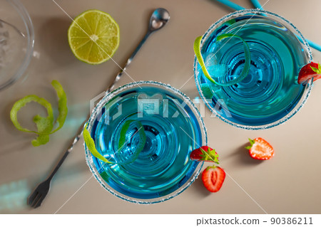 Fresh homemade blue margarita cocktail garnished with lime zest and strawberries Fresh homemade blue margarita cocktail garnished with lime zest and strawberries 90386211
