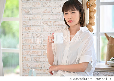 Young woman drinking a drink in a mug in the kitchen Young woman drinking a drink in a mug in the kitchen 90388103