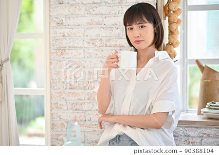 Young woman drinking a drink in a mug in the kitchen Young woman drinking a drink in a mug in the kitchen 90388104