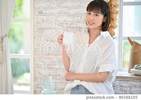 Young woman drinking a drink in a mug in the kitchen Young woman drinking a drink in a mug in the kitchen 90388105
