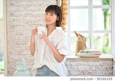Young woman drinking a drink in a mug in the kitchen Young woman drinking a drink in a mug in the kitchen 90388109