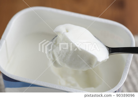 Scoop plain yogurt in a pack container with a spoon and eat 90389096