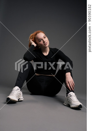 Smiling redhead young sportswoman resting on floor in studio 90390182
