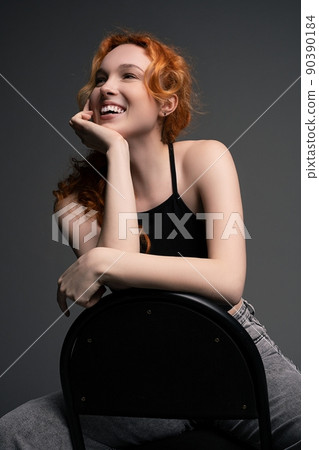 Delighted young lady sitting on chair leaning on hand and smiling 90390184