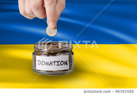 Donation for Ukraine concept. Help and financial assistance to Ukraine. donation jar with Ukrainian flag. Ukrainian war, donations, Hand putting Coins in glass jar with donation 90391088