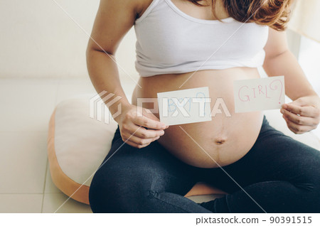 Cropped shot view of pregnant woman show a paper write words "Boy" or "Girl" for asking someone about her child gender. 90391515