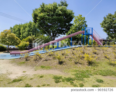 There is a pink slide in the park. The blue sky is very beautiful in the background. 90392726