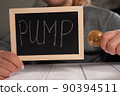 Close-up of a woman holding a board with the inscription PUMP and a gold bitcoin 90394511