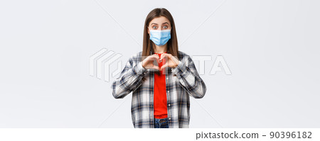 Different emotions, covid-19 pandemic, coronavirus self-quarantine and social distancing concept. Excited young woman in medical mask making confession, show heart sign like someone, express sympathy 90396182