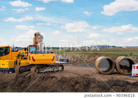 Many heavy industrial machines big large concrete sewage pipes stack warehouse construction site near Leipzig Halle airport against blue sky background. Highway road construction excavator earthworks 90396818