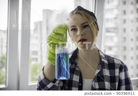 The hostess sprays glass cleaner on the window. The concept of cleanliness in the house. 90396911