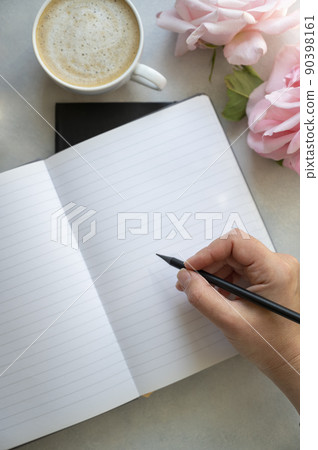 Open note book and female hands holding a pencil. Empty page mockup, cup of coffee, pink roses flowers on bright background. Table top, to do list. 90398161