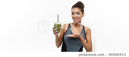 Healthy and Fitness concept - Beautiful American African lady in fitness clothing drinking healthy vegetable drink. Isolated on white background. Healthy and Fitness concept - Beautiful American African lady in fitness clothing drinking healthy vegetable drink. Isolated on white background. 90400413