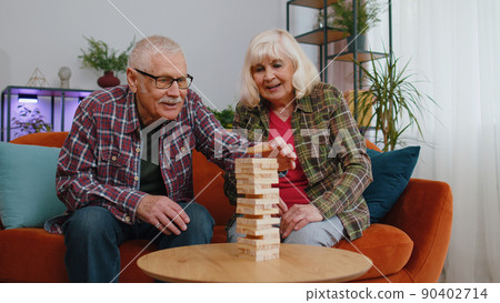 Senior old grandparents man woman playing in blocks wooden tower build board game on table at home Senior old grandparents man woman playing in blocks wooden tower build board game on table at home 90402714