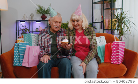 Happy senior family man woman celebrating birthday anniversary hold cupcake makes wish at home 90402799