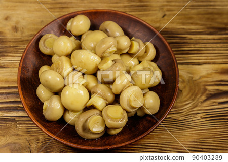 Ceramic plate with pickled champignons. Marinated mushrooms on wooden table 90403289