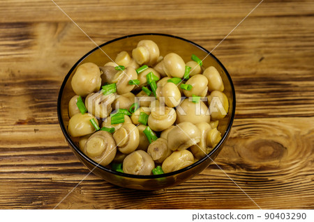 Glass bowl with pickled champignons. Marinated mushrooms on wooden table 90403290