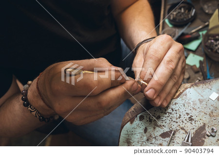 A jeweler is taking apart a gold ring with stones in a workshop, close-up 90403794