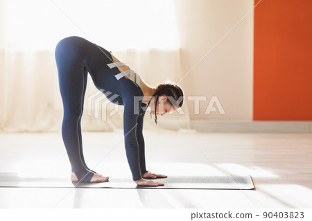 An attractive woman practicing yoga, performing the exercise of Ardha uttanasana, standing with a forward tilt, training in blue sportswear indoors An attractive woman practicing yoga, performing the exercise of Ardha uttanasana, standing with a forward tilt, training in blue sportswear indoors 90403823