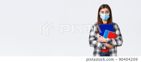 Coronavirus pandemic, covid-19 education, and back to school concept. Surprised female student in medical mask look amazed, widen eyes from big news, carry notebooks, white background 90404209