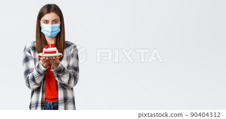 Coronavirus outbreak, lifestyle during social distancing and holidays celebration concept. Cute young woman in medical mask celebrating birthday alone during quarantine, hold b-day cake Coronavirus outbreak, lifestyle during social distancing and holidays celebration concept. Cute young woman in medical mask celebrating birthday alone during quarantine, hold b-day cake 90404312