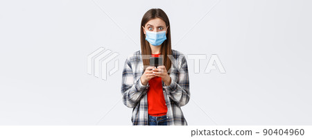 Different emotions, covid-19, social distancing and technology concept. Puzzled and confused young woman in medical mask react to strange message, hold mobile phone, look camera unsure 90404960