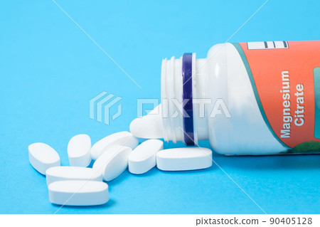 Magnesium citrate pills spill out of a jar on a blue background. Magnesium citrate pills spill out of a jar on a blue background. 90405128