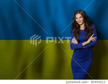 Happy young woman in blue dress smiling against Ukrainian flag background Happy young woman in blue dress smiling against Ukrainian flag background 90405612