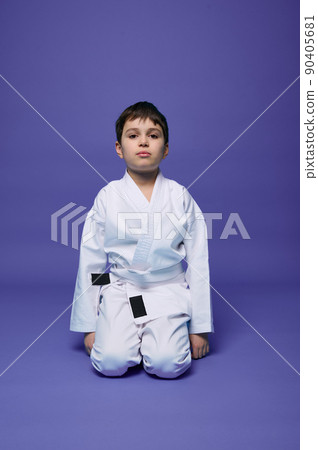 Portrait of a handsome child boy wearing kimono and sitting in aikido stance against purple background with copy space for text. Oriental martial arts concept Portrait of a handsome child boy wearing kimono and sitting in aikido stance against purple background with copy space for text. Oriental martial arts concept 90405681