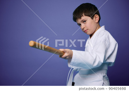 Waist length portrait of a confident teenage boy in white kimono practices wooden bokken in Aikido training on purple background with copy ad space 90405698