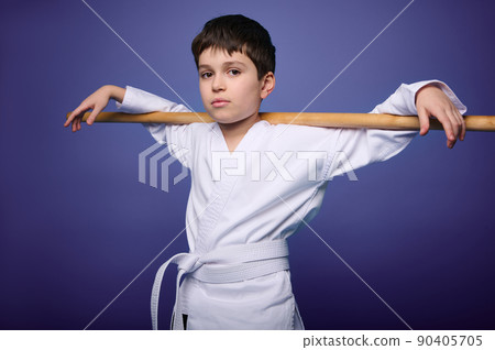 Confident strong Caucasian Oriental martial arts wrestler posing with wooden aikido weapon against violet background with copy ad space Confident strong Caucasian Oriental martial arts wrestler posing with wooden aikido weapon against violet background with copy ad space 90405705