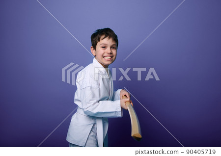 Smiling teenage boy in white kimono practices sword in Aikido training on purple background, copy ad space. Concepts of Oriental martial arts practice Smiling teenage boy in white kimono practices sword in Aikido training on purple background, copy ad space. Concepts of Oriental martial arts practice 90405719