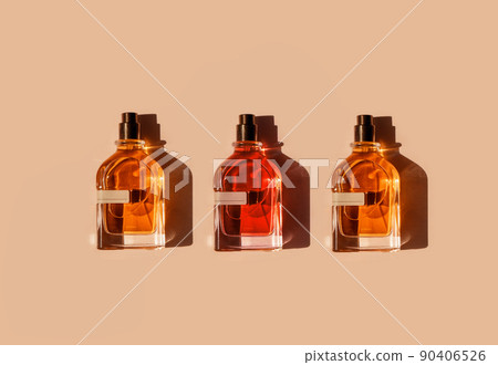 Three different perfume bottles on a pastel beige background in the sunlight. Flat lay, top view. Luxury presentation mockup. Red, yellow and orange samples of aroma water 90406526
