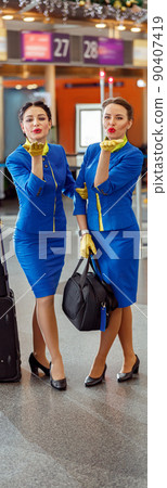 Two women stewardesses blowing kiss at airport terminal 90407419