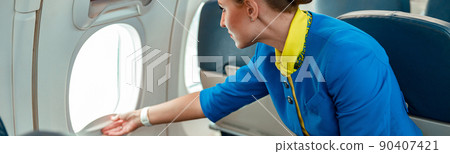Female flight attendant opening window in airplane 90407421