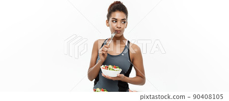 Healthy and Fitness concept - Beautiful American African lady in fitness clothes on diet eating fresh salad. Isolated on white background. Healthy and Fitness concept - Beautiful American African lady in fitness clothes on diet eating fresh salad. Isolated on white background. 90408105