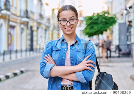 Confident teenage girl in glasses with backpack looking at camera outdoor Confident teenage girl in glasses with backpack looking at camera outdoor 90408299