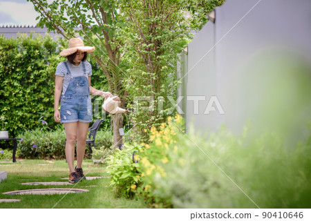 An Asian woman is watering plants in the garden. An Asian woman is watering plants in the garden. 90410646