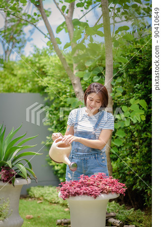 An Asian woman is watering plants in the garden. 90410649