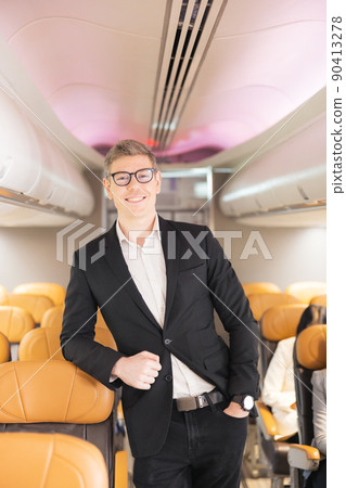 In the plane, there is a young passenger. portrait of a man standing in an airplane aisle In the plane, there is a young passenger. portrait of a man standing in an airplane aisle 90413278