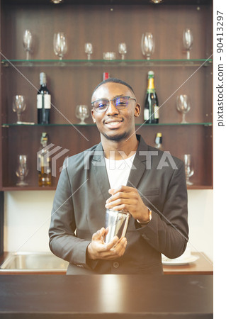 Making a beverage, a black handsome bartender smiles at the camera. Making a beverage, a black handsome bartender smiles at the camera. 90413297