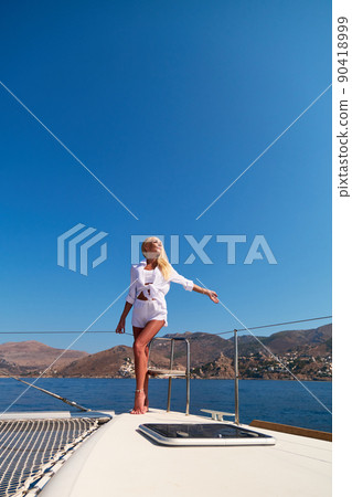 Beautiful young blond woman in bikini standing on catamaran at sunny summer day Beautiful young blond woman in bikini standing on catamaran at sunny summer day 90418999