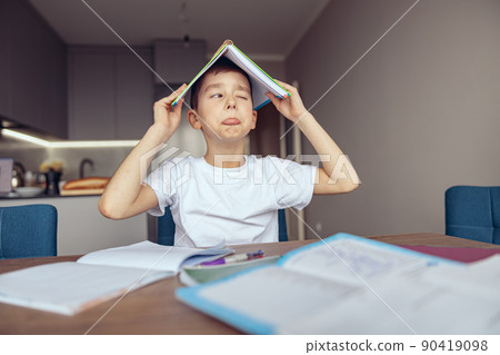 Cute funny small Caucasian teen schoolboy holding book above head and mocking. Lazy,homework. Cute funny small Caucasian teen schoolboy holding book above head and mocking. Lazy,homework. 90419098