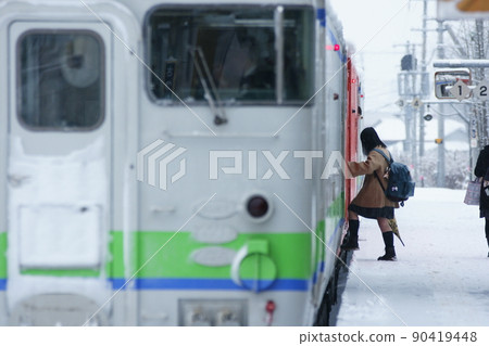 A high school girl boarding a regular train at Satsunai Station in the snow 90419448