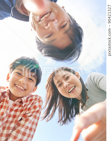 A family of three looking into the camera with a smile under the blue sky 90421327